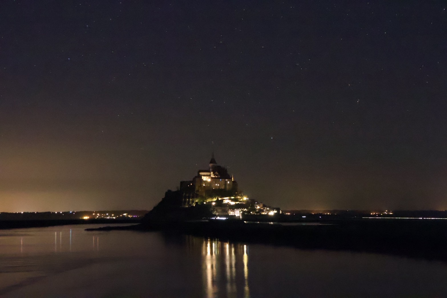 夜の星空とライトアップされ水面に映り込むモンサンミッシェルの夜景
