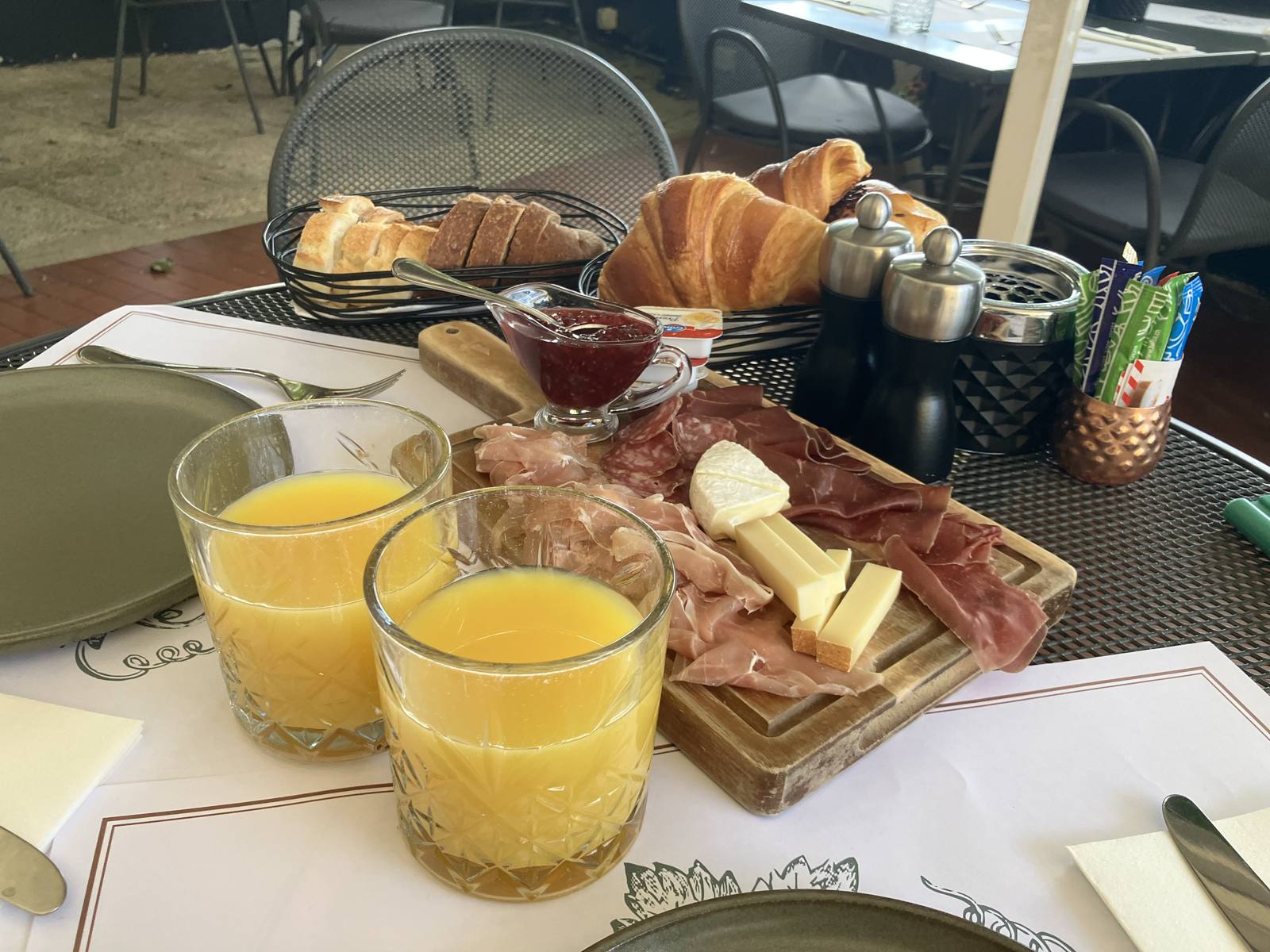 朝食。オレンジジュースと生ハム・チーズのボード、パンのバスケット