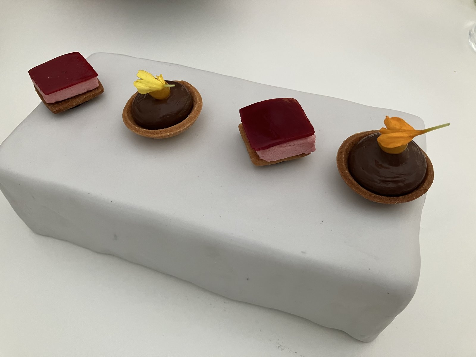 食後の小菓子。ベリーのムースとチョコレートのタルトレットが食用花とともに並ぶ