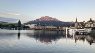 朝焼けのルツェルン。湖の向こうに朝日で赤く染まるピラトゥス山