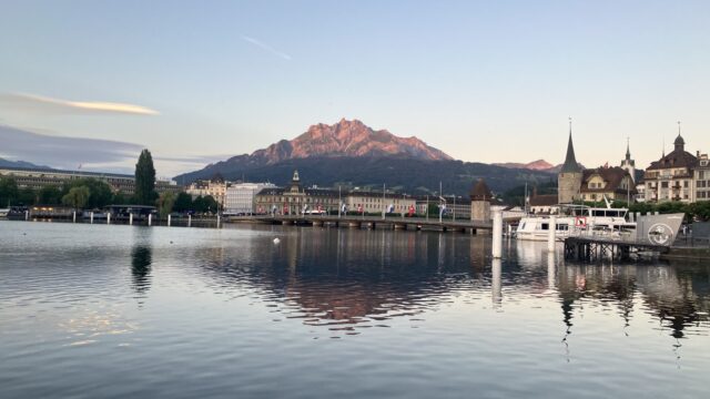 朝焼けのルツェルン。湖の向こうに朝日で赤く染まるピラトゥス山