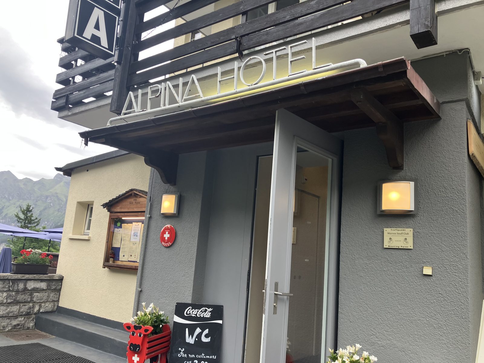 ホテル・アルピナのエントランス。ALPINA HOTELの看板と赤い牛のプランター