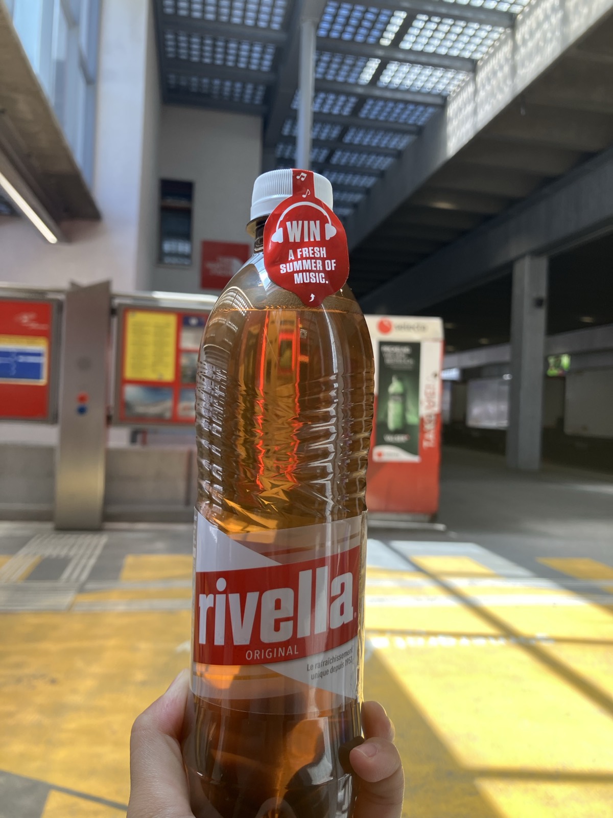 Rivella Originalのペットボトルを手に持つ。駅のホームで