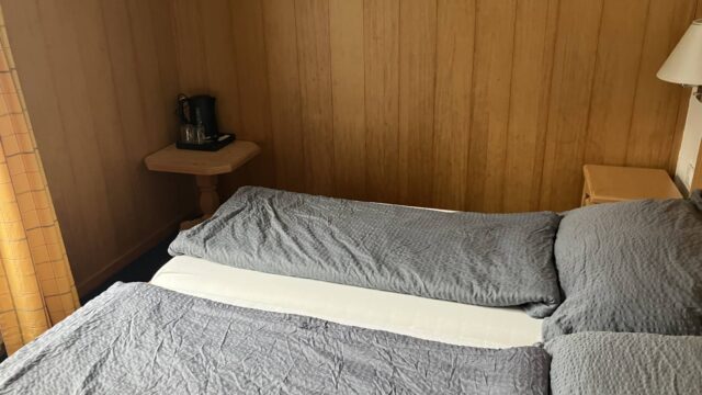 ホテル・ヘルヴェティアの客室。木のパネル壁とベッド2台、脇のテーブルにケトル